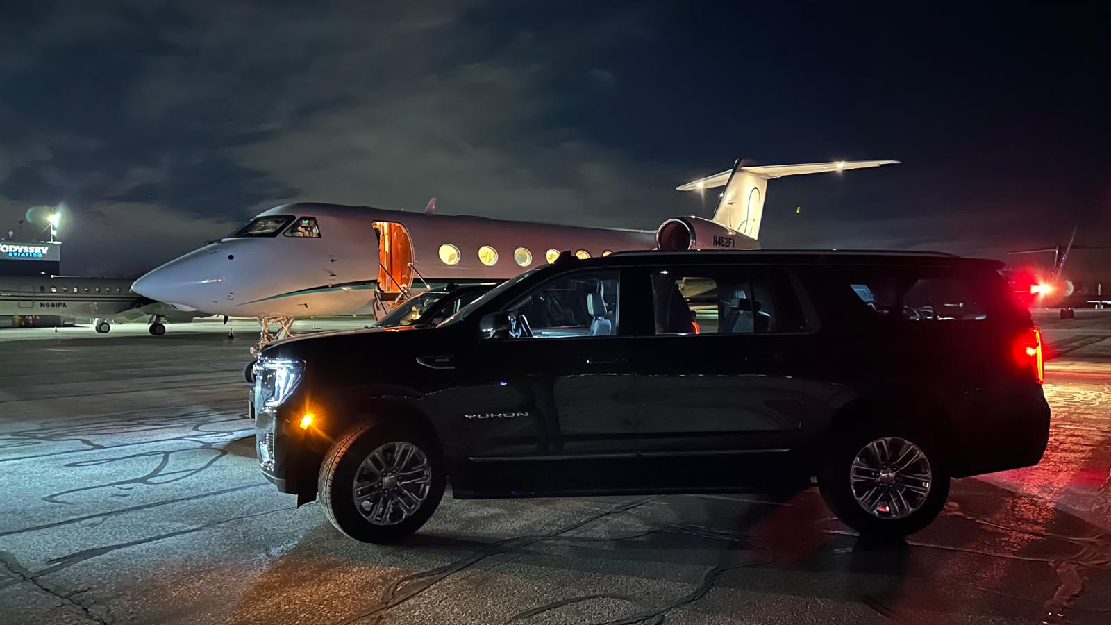 LuxeDetroit SUV on the tarmac beside a private jet at night
